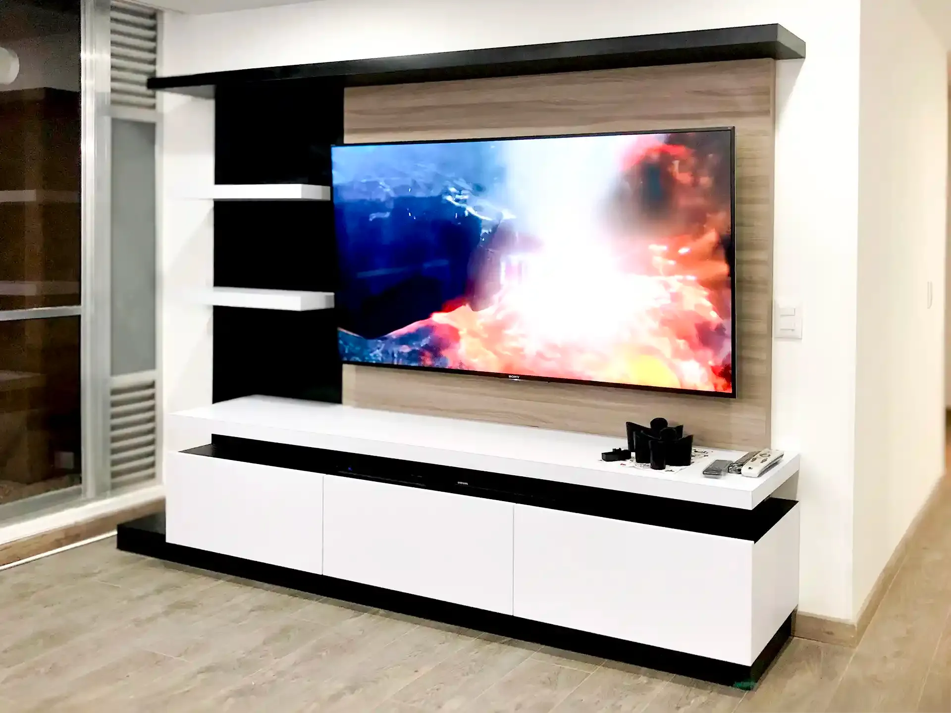 Centro de entretenimiento con TV, panel, mueble bajo y repisas laterales