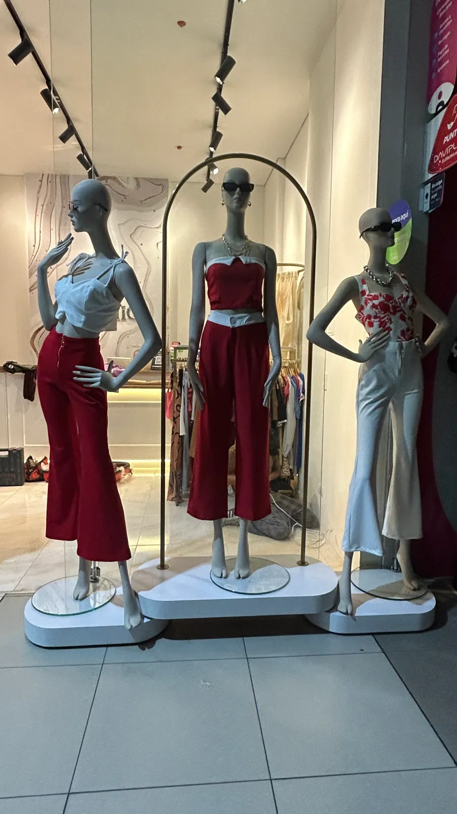 Exhibición comercial de maniquíes sobre bases, con un arco metálico y un panel de fondo.