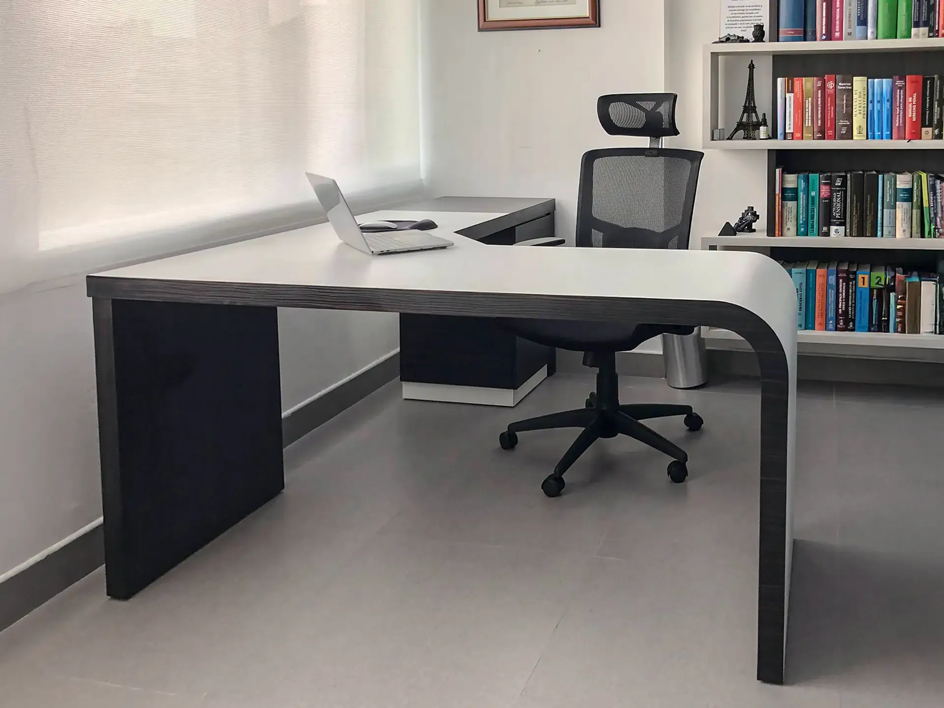 Escritorio de oficina en L con superficie amplia y biblioteca al fondo