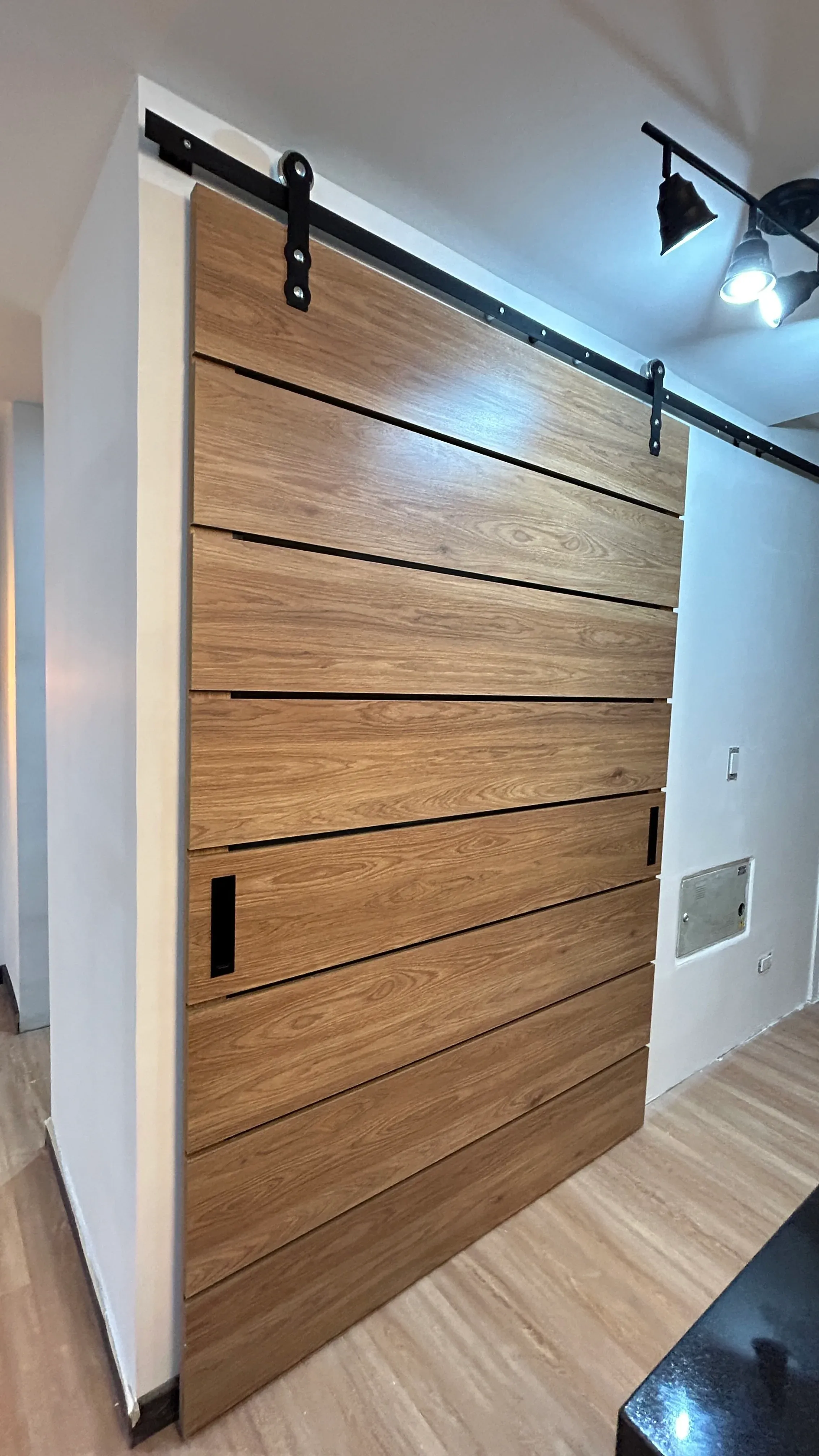 Puerta corredera estilo granero con rieles industriales expuestos para ahorro de espacio.