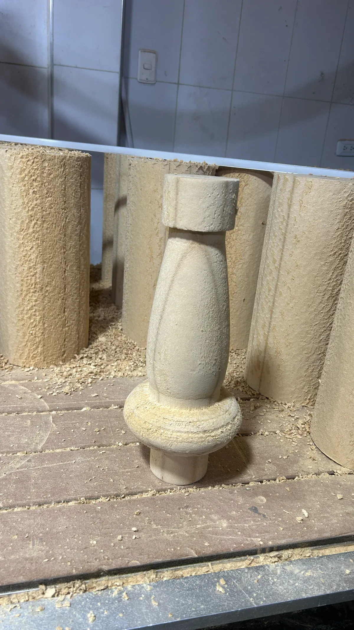 Pieza de madera con perfil torneado sobre la mesa de trabajo, junto a componentes en proceso