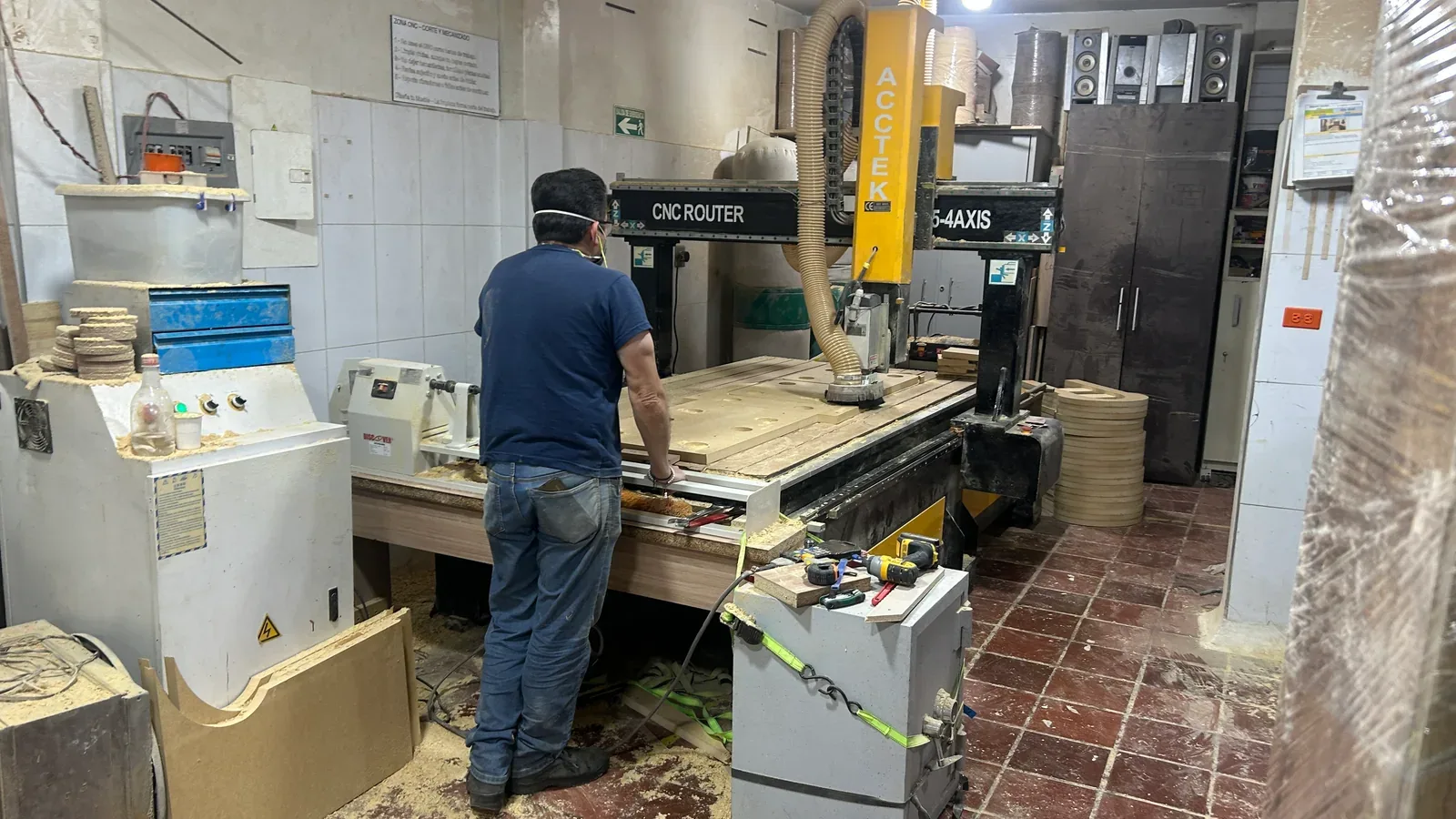 Operario junto a un router CNC y tablero con cortes circulares en la mesa de trabajo